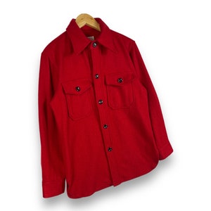 May include: A red long-sleeved shirt with a button-up front and two flap pockets. The shirt is made of a thick, textured fabric.
