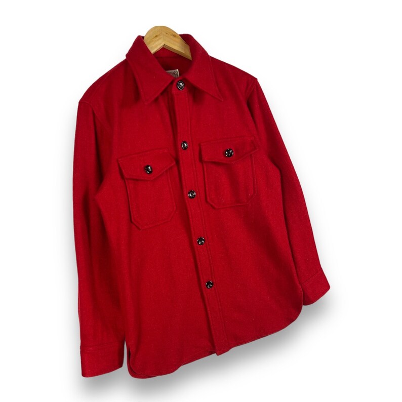 May include: A red long-sleeved shirt with a button-up front and two flap pockets. The shirt is made of a thick, textured fabric.