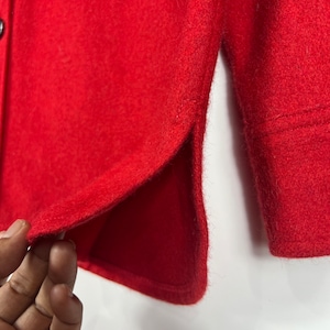 May include: A close-up of a red button-up shirt with a single button visible. The shirt has a side seam detail and is made of a soft, textured fabric.