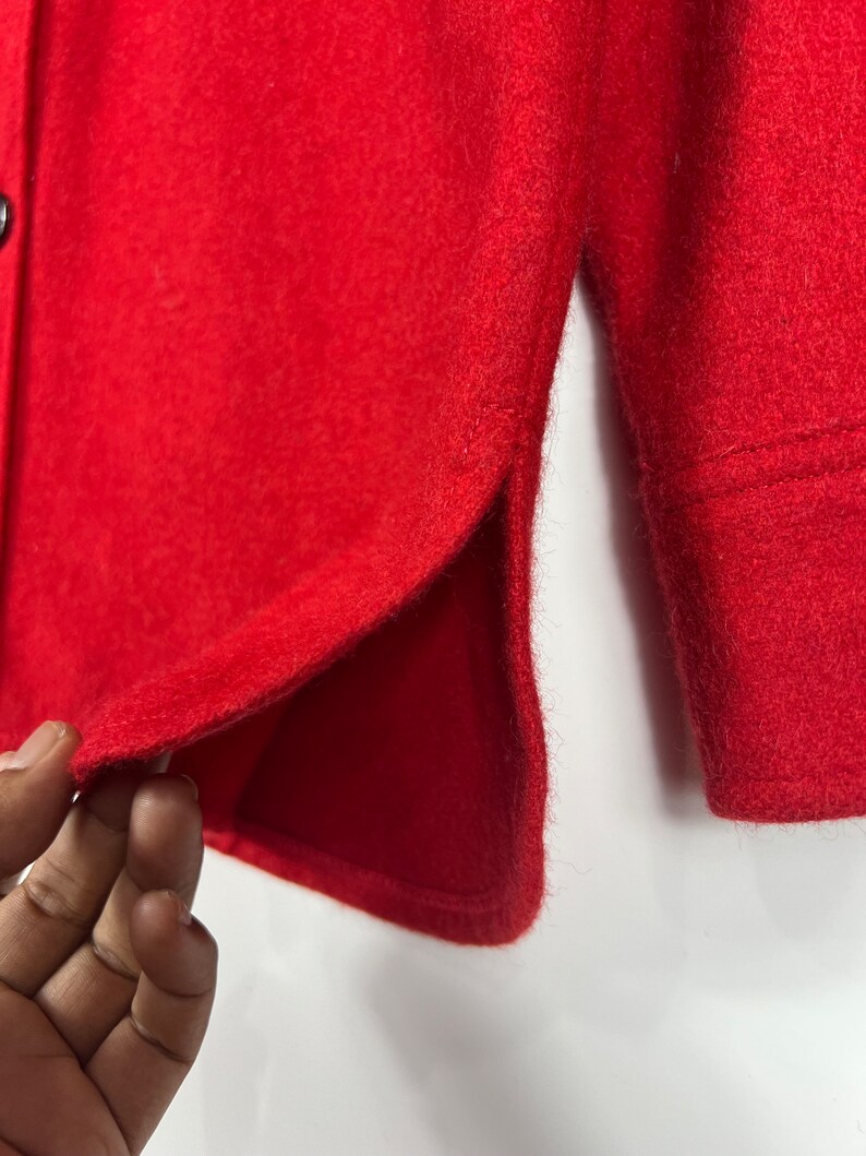 May include: A close-up of a red button-up shirt with a single button visible. The shirt has a side seam detail and is made of a soft, textured fabric.