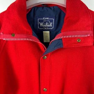 May include: Red wool jacket with a navy blue lining and a label that reads "THE Woolrich EST 1830 WOMAN".