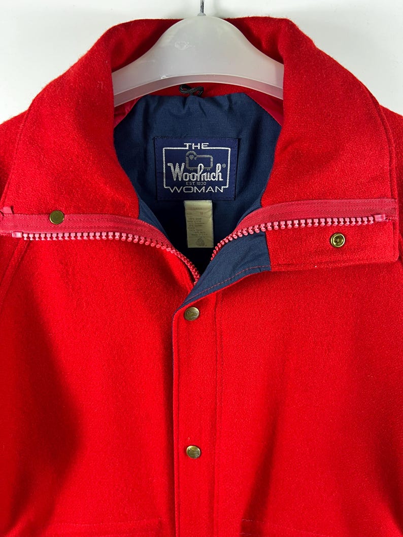 May include: Red wool jacket with a navy blue lining and a label that reads "THE Woolrich EST 1830 WOMAN".
