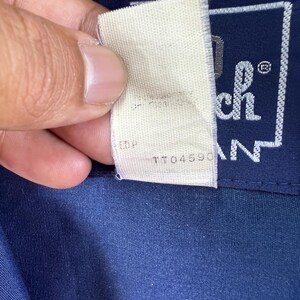 May include: A white tag with the text "TTO4590" and "EDP" on it. The tag is attached to a navy blue shirt with a white patch that says "Tech" in a square.
