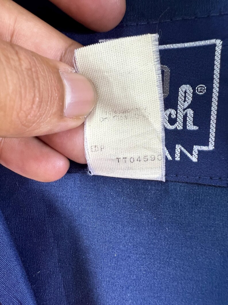 May include: A white tag with the text "TTO4590" and "EDP" on it. The tag is attached to a navy blue shirt with a white patch that says "Tech" in a square.