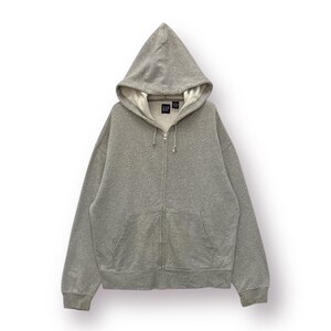 Peut inclure: Un sweat à capuche gris clair avec fermeture éclair et poches avant. Le sweat à capuche est doté d'une fermeture éclair complète et du logo GAP sur la poitrine. L'intérieur du capuchon est d'une couleur plus claire.