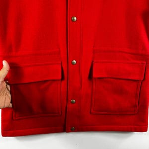 May include: A red wool jacket with a button closure and two large flap pockets on the front.