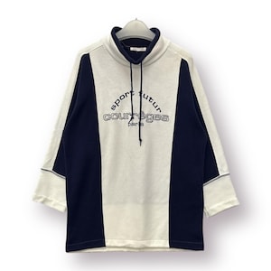 Puede incluir: Una sudadera crema y azul marino con el texto "sport futur courr&egrave;ges paris". La sudadera tiene un cuello alto con cord&oacute;n y mangas tres cuartos. El dise&ntilde;o presenta paneles azul marino en los laterales.