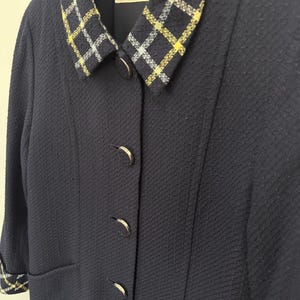 May include: A navy blue jacket with a textured fabric. The jacket features a plaid collar with yellow and white accents. The jacket has four silver buttons and a small pocket. The label reads "courr&egrave;ges paris".