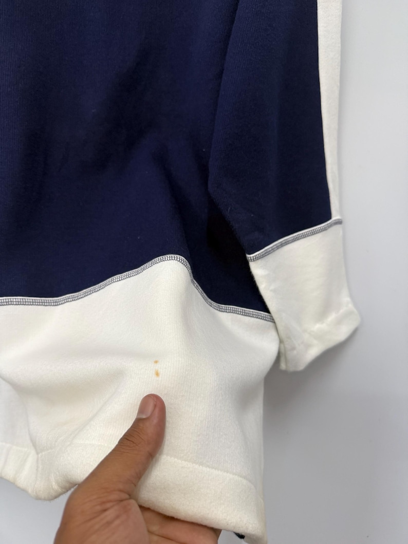 Puede incluir: Una sudadera azul marino y crema. La sudadera presenta un dise&ntilde;o de bloques de color con azul marino en la parte superior y crema en la inferior. Los pu&ntilde;os de las mangas son crema con ribete azul marino.