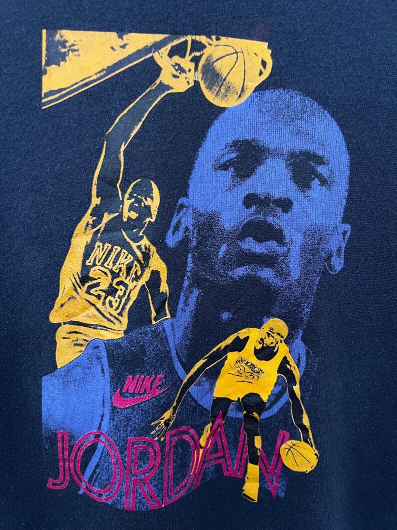 Puede incluir: Sudadera azul marino con un gr&aacute;fico de baloncesto. El dise&ntilde;o presenta a un jugador de baloncesto en acci&oacute;n, la palabra "JORDAN" en ne&oacute;n rosa y el logotipo de Nike. La imagen incluye un retrato de un jugador de baloncesto.