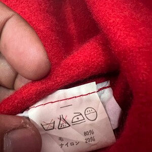 May include: A white care label with black text and symbols. The label shows washing instructions, including a symbol for no washing, a symbol for dry cleaning, a symbol for ironing, and a symbol for tumble drying. The label also shows the fabric composition: 80% wool and 20% nylon.