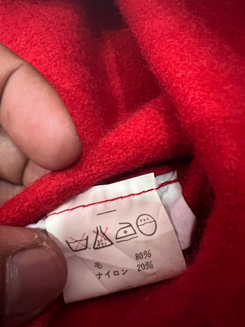 May include: A white care label with black text and symbols. The label shows washing instructions, including a symbol for no washing, a symbol for dry cleaning, a symbol for ironing, and a symbol for tumble drying. The label also shows the fabric composition: 80% wool and 20% nylon.