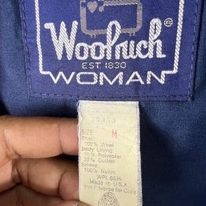 May include: A close-up of a beige tag with black text. The tag says "Size M" and lists the fabric content of the jacket. The tag also says "WPL 5635" and "Made in USA".