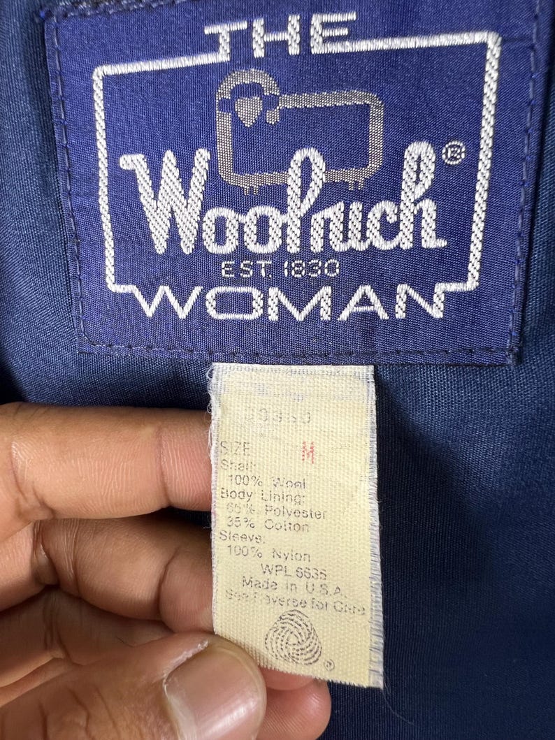 May include: A close-up of a beige tag with black text. The tag says "Size M" and lists the fabric content of the jacket. The tag also says "WPL 5635" and "Made in USA".