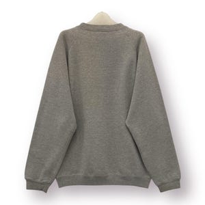 Pode incluir: Um moletom cinza mesclado com gola redonda e mangas compridas. A parte de tr&aacute;s da pe&ccedil;a &eacute; vis&iacute;vel, pendurada em um cabide branco sobre um fundo branco. O moletom tem um design simples e cl&aacute;ssico.