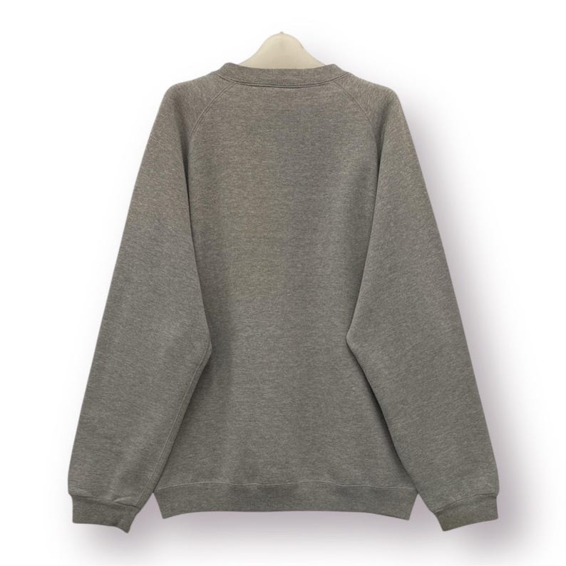 Pode incluir: Um moletom cinza mesclado com gola redonda e mangas compridas. A parte de tr&aacute;s da pe&ccedil;a &eacute; vis&iacute;vel, pendurada em um cabide branco sobre um fundo branco. O moletom tem um design simples e cl&aacute;ssico.