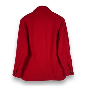May include: A red long-sleeved shirt made of wool. The shirt has a button-up front and a collared neckline.
