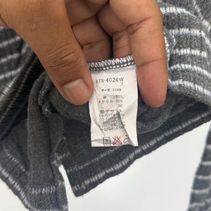 May include: A dark gray garment with light gray horizontal stripes and a white interior care label. The label displays the text ATN-4024 W, size 11(40), 50% cotton, 50% acrylic, and various Japanese characters including manufacturer contact information.