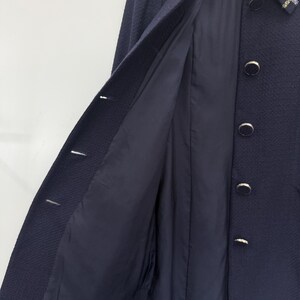 May include: A navy blue coat with a textured weave, featuring a contrasting plaid collar and gold-toned buttons. The coat's interior lining is a solid navy blue. The Courr&egrave;ges logo is visible on the collar.