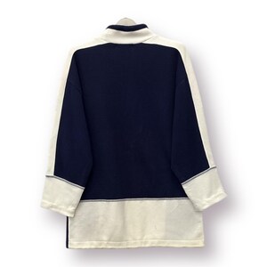 Puede incluir: Una camisa de manga larga azul marino y crema. La camisa presenta un cuello alto y paneles de color crema en las mangas y el dobladillo inferior. Las mangas tienen un ribete gris. La camisa est&aacute; hecha de un material suave.