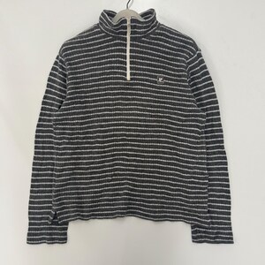 May include: A charcoal gray and white horizontally striped long-sleeve pullover sweater with a ribbed texture. The garment features a high collar with a white front zipper closure and a small square logo patch on the left chest area.