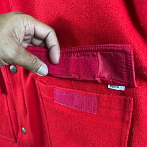 May include: Red fleece jacket with a large pocket on the front. The pocket has a velcro closure and a label that says "MEDIUM".