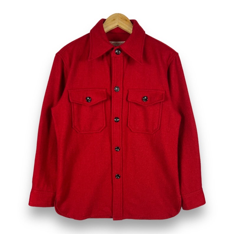 May include: A red long-sleeved button-up shirt with two large flap pockets and black buttons.