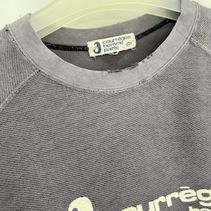 May include: A gray crew neck sweatshirt with the brand name "courr&egrave;ges homme paris" printed on the front. The sweatshirt has a distressed look, with a worn collar and a faded logo.