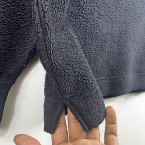 Op de afbeelding: Close-up van de zwarte fleece stof van een sweatshirt. De stof heeft een zachte, pluche textuur.
