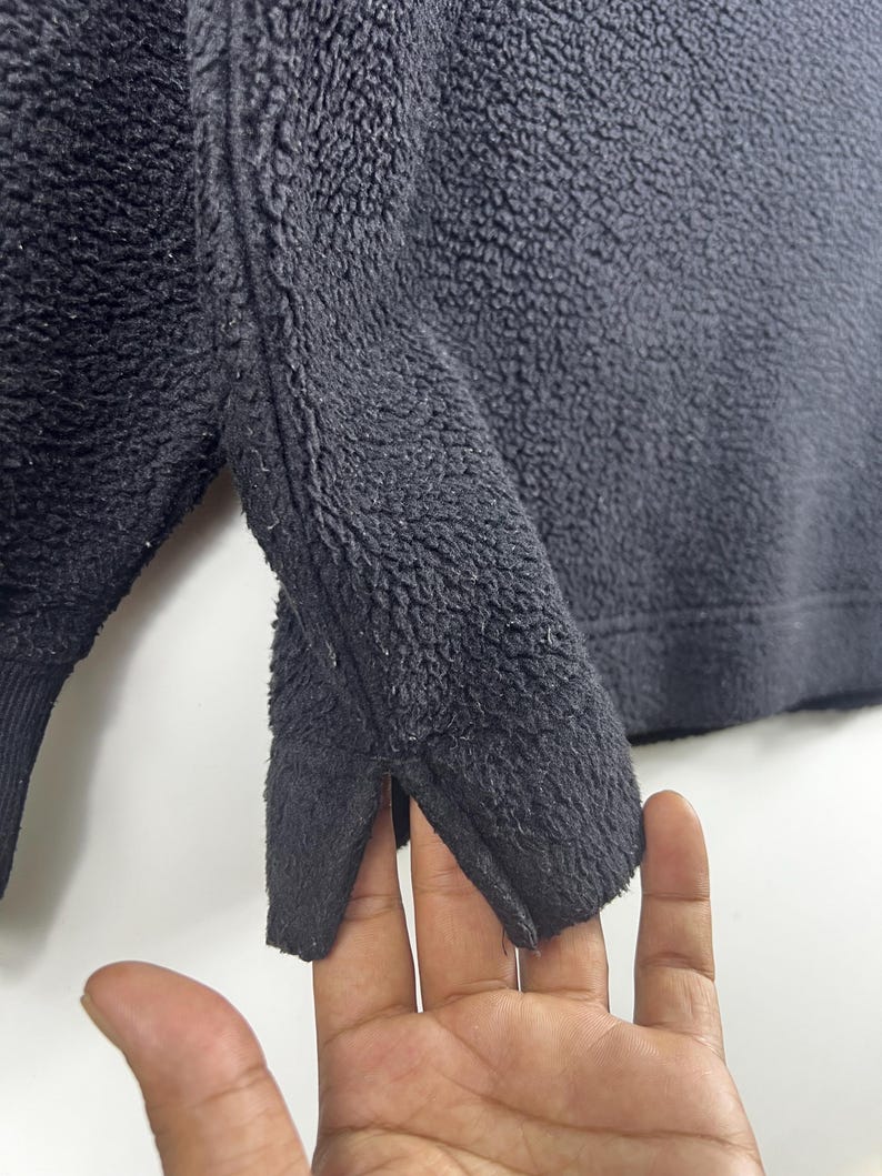 Op de afbeelding: Close-up van de zwarte fleece stof van een sweatshirt. De stof heeft een zachte, pluche textuur.