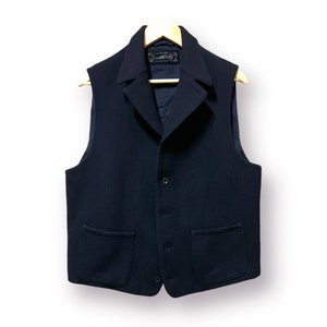 Könnte beinhalten: Eine dunkelblaue Wollweste mit einem V-Ausschnitt, zwei vorderen Taschen und einem Knopfverschluss. Die Weste hat ein Etikett mit der Aufschrift "ZARA B.B."