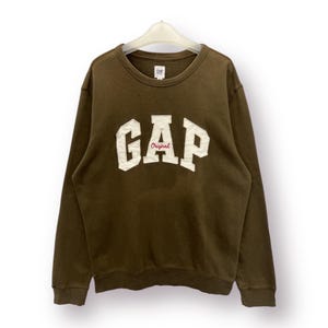 Peut inclure: Un sweat-shirt marron avec un logo "GAP Original" blanc sur le devant.