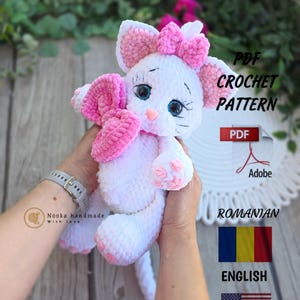 Può includere: Una bambola a forma di gatto all'uncinetto bianca e rosa fatta a mano con occhi blu e un fiocco rosa. La bambola è tenuta davanti a uno sfondo con il testo "PDF Crochet Pattern" e le bandiere di Romania e Stati Uniti.
