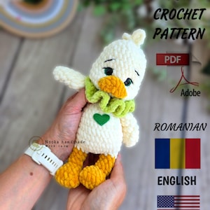 May include: A handmade, plush duck toy in cream, yellow, and green. The duck has a green scarf, a heart, and a yellow beak and feet. The image includes text that says "PDF Crochet Pattern" and "English".