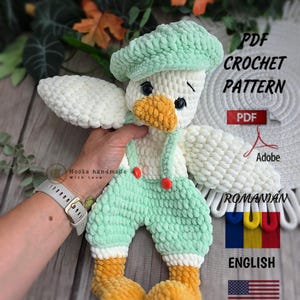 May include: A plush crochet duck toy featuring a white body, orange beak and feet, and light green overalls with red buttons and a matching beret. The image includes text stating PDF CROCHET PATTERN, Adobe, ROMANIAN, and ENGLISH with flag icons.