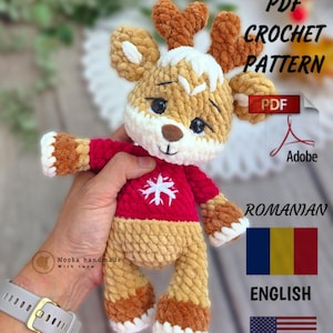 Op de afbeelding: Een gehaakt rendier speelgoed met een rode trui en een witte sneeuwvlok. Het rendier heeft bruine geweien, een witte snuit en een bruin lichaam. De afbeelding bevat de tekst "PDF Crochet Pattern" en "English".
