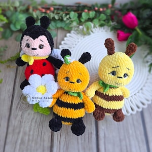 May include: Three handmade crochet plush toys: a ladybird, a bee, and another bee. The ladybird is red and black with a white flower. The bees are yellow and brown with black stripes and antennae. Each has a green scarf.