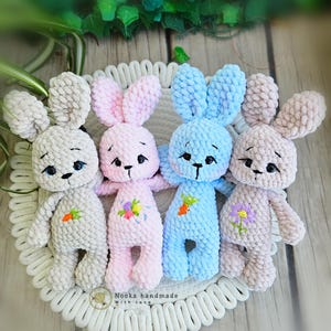 Puede incluir: Cuatro peluches de conejo de crochet en diferentes colores: gris, rosa, azul y beige. Cada conejo tiene detalles bordados, incluidos ojos, nariz y boca. Los conejos est&aacute;n sentados en una alfombra de crochet blanca.