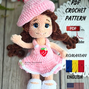 May include: A crocheted doll in a pink dress and beret, with brown hair and blue eyes. The dress features a strawberry design. The image includes text that says "PDF Crochet Pattern" and "English".