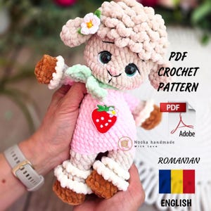 Può includere: Bambola di agnello all'uncinetto con vestito rosa e applicazione a fragola. L'agnello ha una texture riccia marrone chiaro, una sciarpa verde e un fiore. L'immagine include il testo "PDF Crochet Pattern".