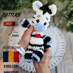 Könnte beinhalten: Häkelanleitung für ein Zebra-Amigurumi-Spielzeug. Die Anleitung ist sowohl in englischer als auch in rumänischer Sprache verfügbar. Das Zebra ist schwarz-weiß mit einer blauen Nase und einem roten Herzen auf der Brust. Die Anleitung ist als PDF-Download verfügbar.