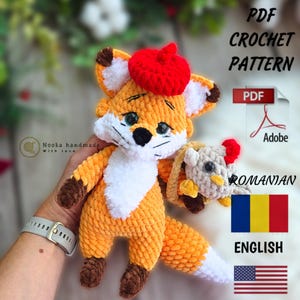 May include: A crocheted orange fox with a white chest and a red beret, holding a smaller crocheted chicken. The image includes text that says "PDF Crochet Pattern" and flags for Romania and the United States.