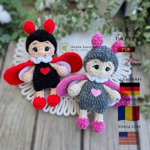 May include: Two handmade crochet dolls, one black and one gray, with red and pink accents. Each doll has a heart on its chest and a white collar. The dolls are displayed on a white, decorative surface.