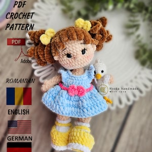 Peut inclure: Patron de crochet PDF pour une poupée aux cheveux bruns portant une robe bleue et tenant un oiseau blanc. Le patron est disponible en roumain, anglais et allemand. "Nooka handmade with love" est écrit sur l'image.