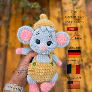 Może przedstawiać: Ręcznie robiona szydełkowa zabawka mysz w kolorze jasnoniebieskim, różowym i żółtym. Mysz ma duże uszy, różowy nos i nosi żółte ogrodniczki i pasujący kapelusz. Obraz zawiera również tekst "PDF CROCHET PATTERN".