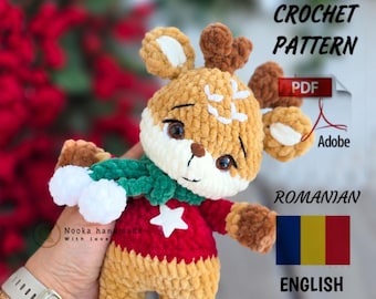 Puede incluir: Un peluche de ganchillo con forma de ciervo en hilo marrón y crema, con un suéter rojo con una estrella blanca y una bufanda verde con pompones blancos. El texto dice PDF CROCHET PATTERN, Adobe, ROMANIAN y ENGLISH con banderas.
