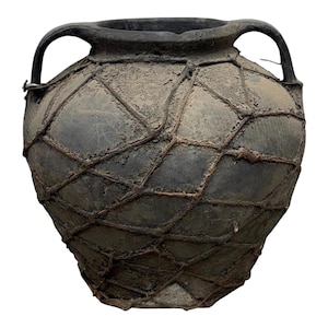 May include: A dark gray, antique-style ceramic vase with two handles. The vase is wrapped in a diamond-patterned netting, giving it a rustic appearance. The surface has a weathered texture, suggesting age and use.