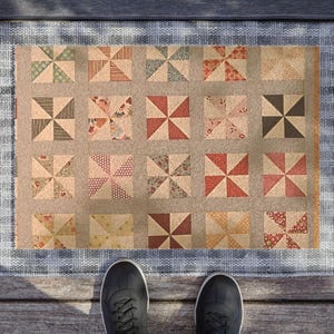 May include: A doormat with a patchwork design featuring a repeating pattern of multicolored pinwheels. The doormat has a light blue border.