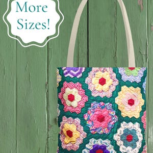May include: A tote bag featuring a colorful patchwork design of hexagonal floral patterns in shades of pink, yellow, purple, and blue on a dark green background, with two beige fabric handles and the text More Sizes! in a white scalloped frame.