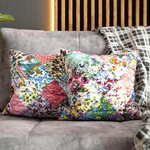 May include: Two square throw pillows featuring a patchwork design composed of various floral and geometric fabric squares in shades of red, blue, green, pink, and white. The pillows have a quilted texture and are arranged side by side.